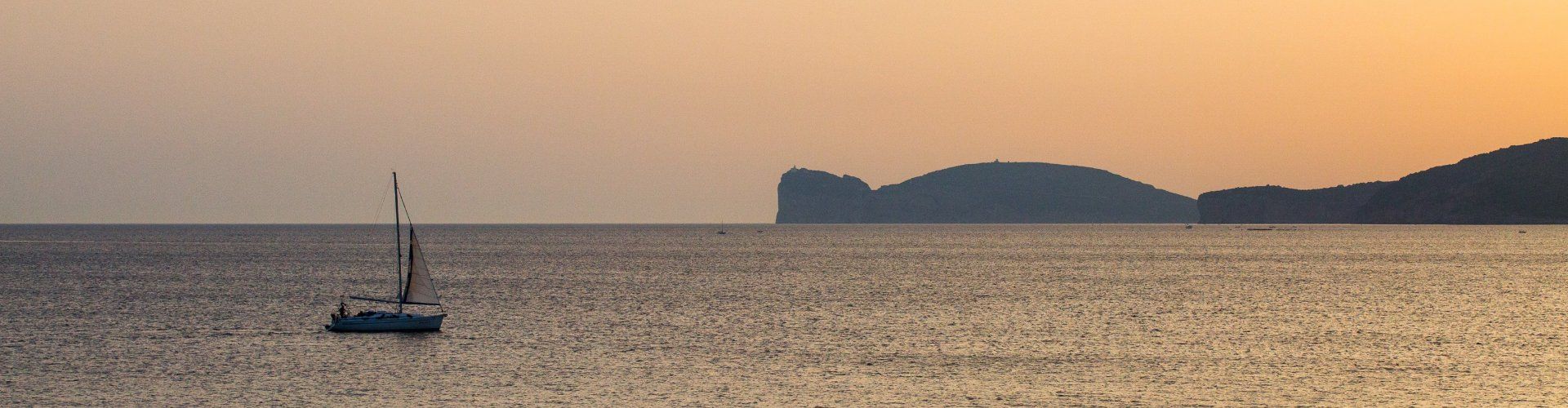 The sea seen from Alghero at sunset with a sailing boat and Capo Caccia on the horizon