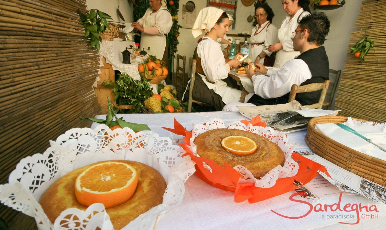 Presentation of orange cakes with the people preparing them in the background, all of them dressed in typical sardinian costumes