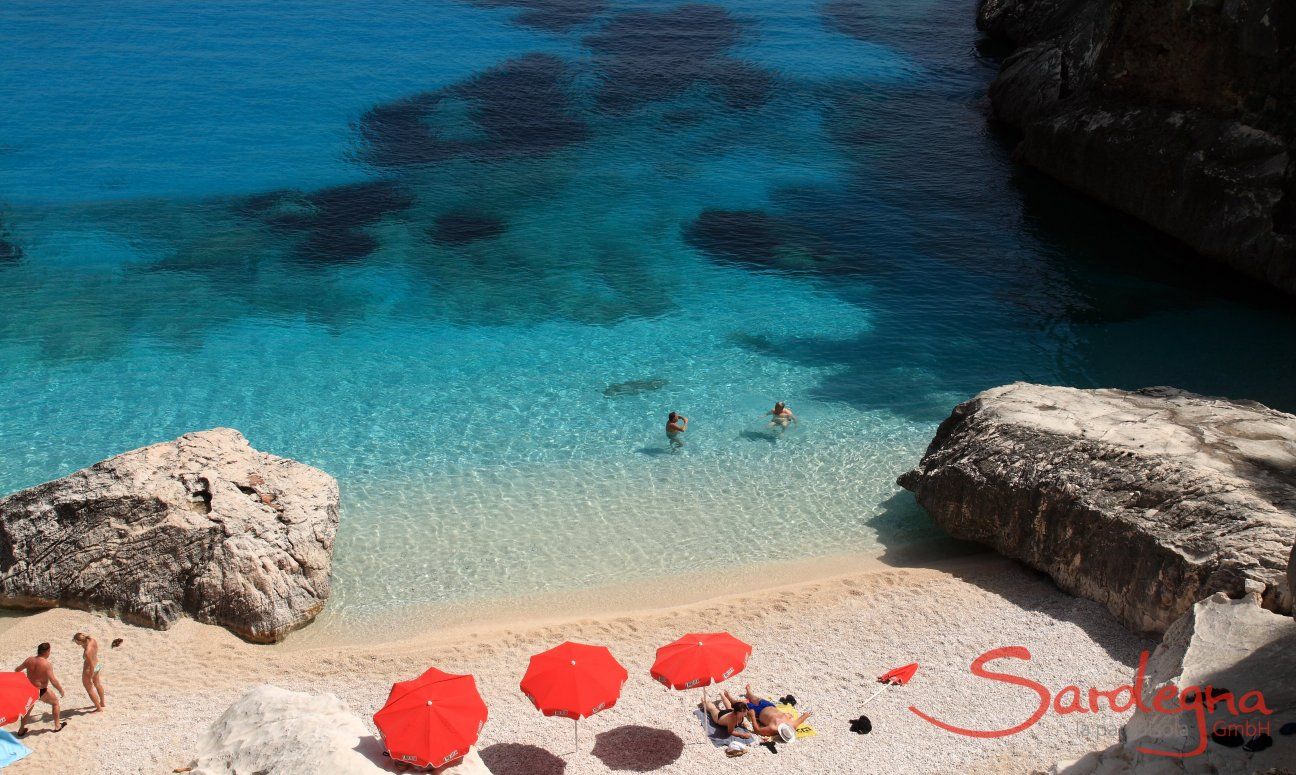 Three red ombrellas offering shade on the white sand beach of Cala Goloritze