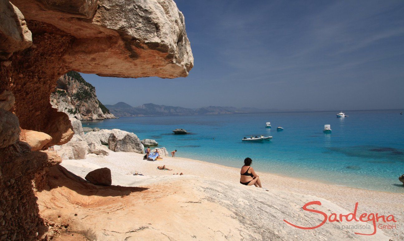 Motorboat Excursions | Cala Luna can be reached only by sea or after a long hike Visitor is sitting on the beach in front of the rocks of Cala Luna and looks over the sea