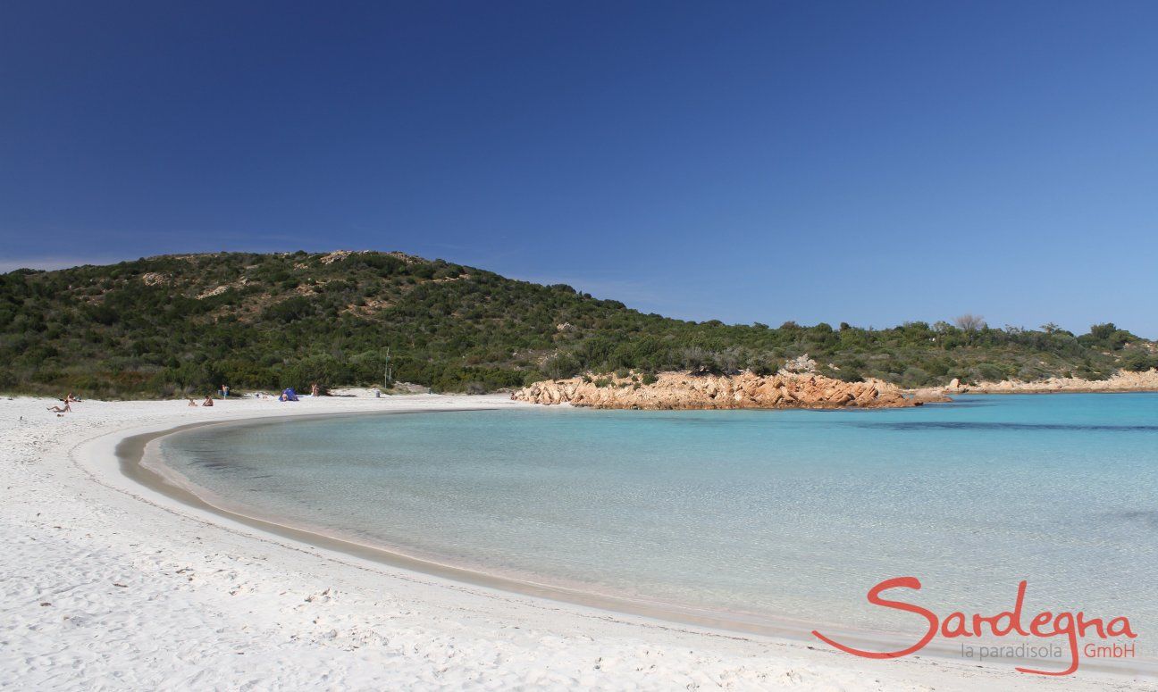 Halfmoon bay of Romazzino with white sand ending in yello coloured rocks and a hill covered in green macchia