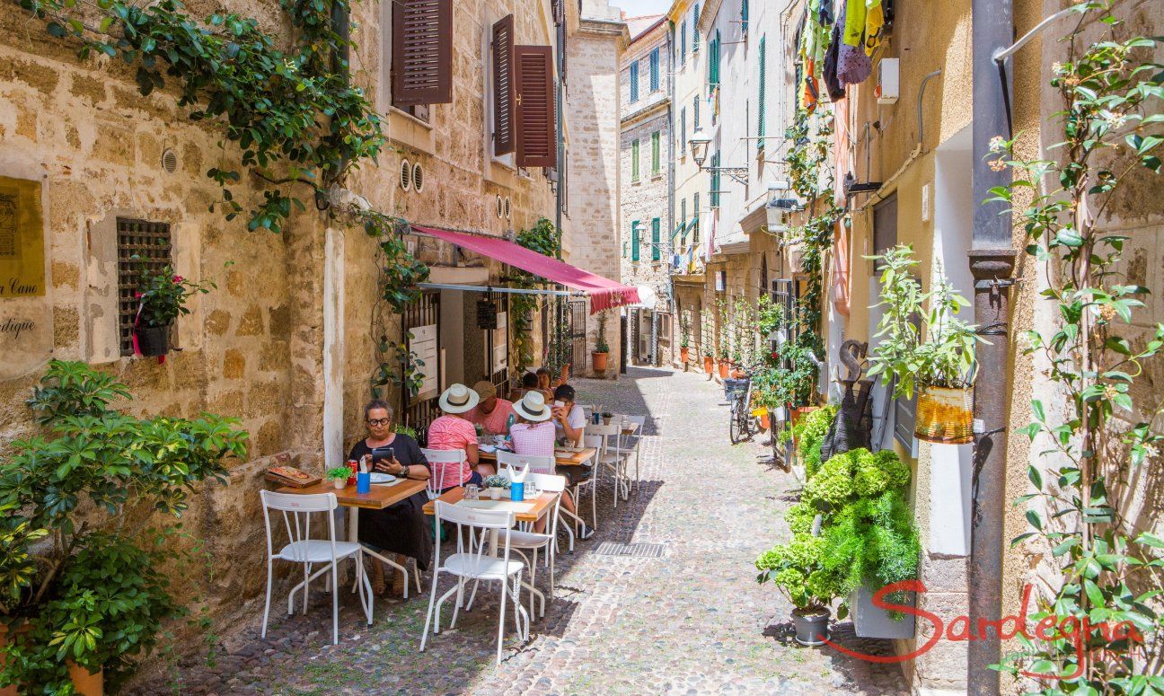 Narrow pedestrian alley of the old town of Alghero with tables of a restaurant to eat outside