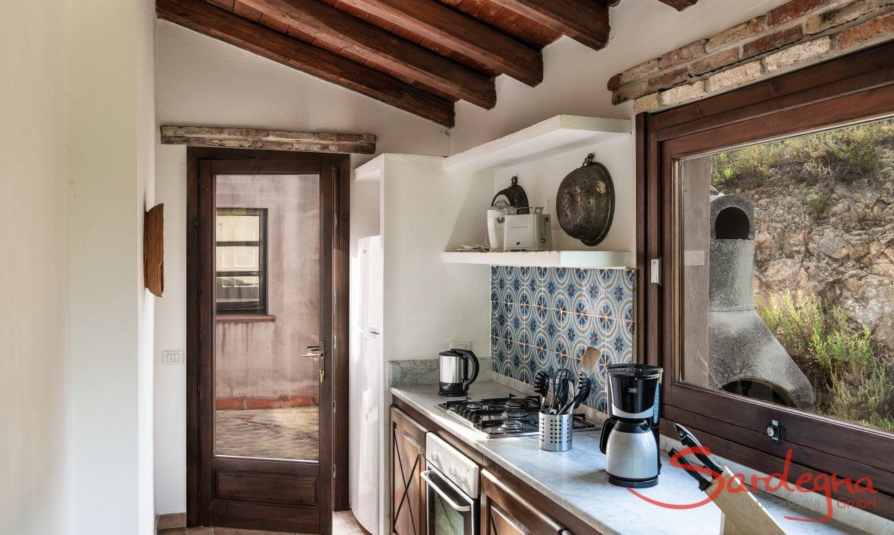 Villa Fiorita | Kitchen with view on the back yard and the brick barbecue Portrait of the villa