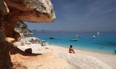 Visitor is sitting on the beach in front of the rocks of Cala Luna and looks over the sea 