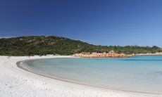 Halfmoon bay of Romazzino with white sand ending in yello coloured rocks and a hill covered in green macchia