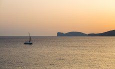 The sea seen from Alghero at sunset with a sailing boat and Capo Caccia on the horizon