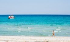 A woman walks on the white sand beach of La Cinta with the light blue sea with a boat in the background